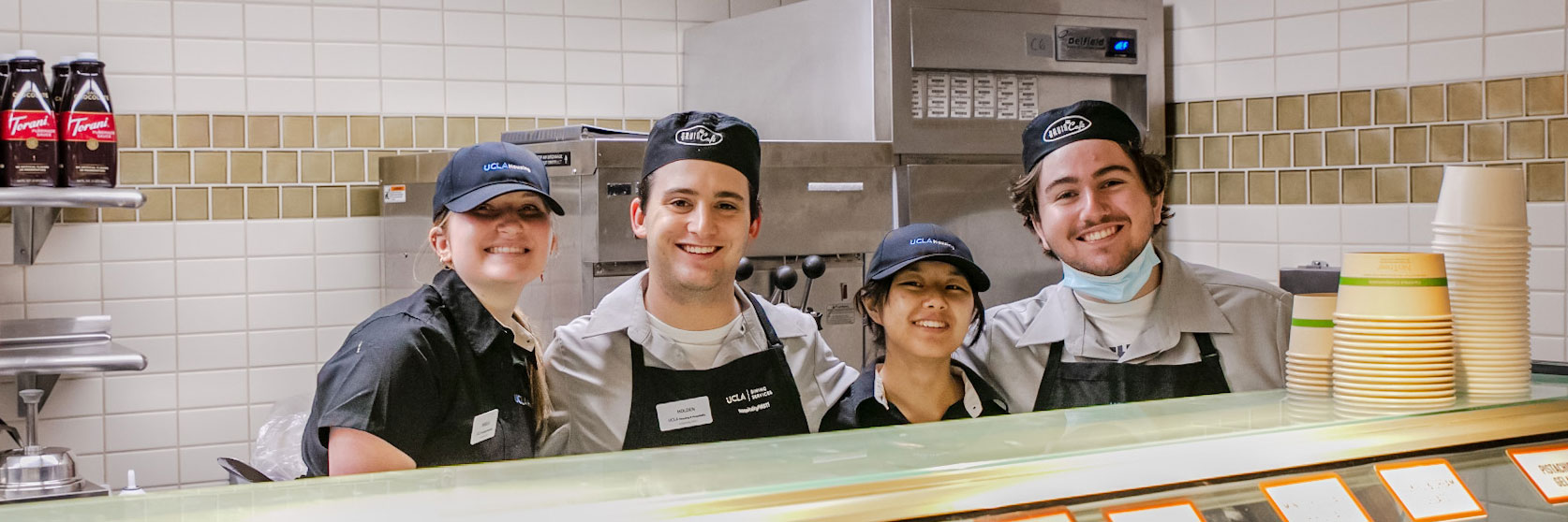 Four smiling student workers enjoying the benefits of working in UCLA Dining